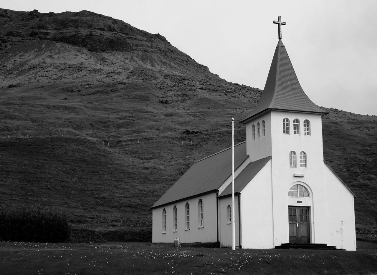 Minimalist black and white photo of a rural church set against a dramatic mountainous backdrop.