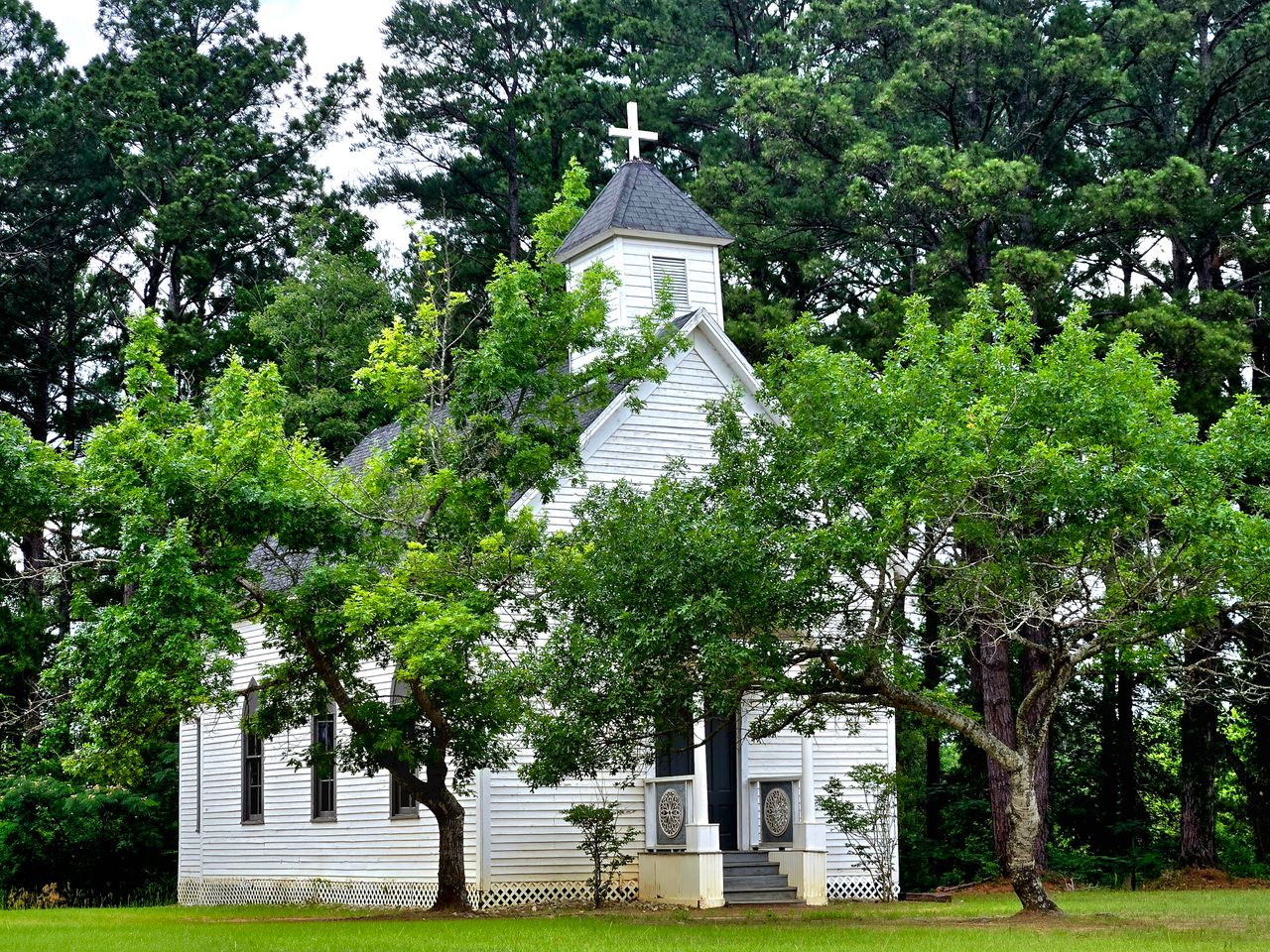 A quaint white church with a steeple surrounded by lush green trees, exuding a serene atmosphere.