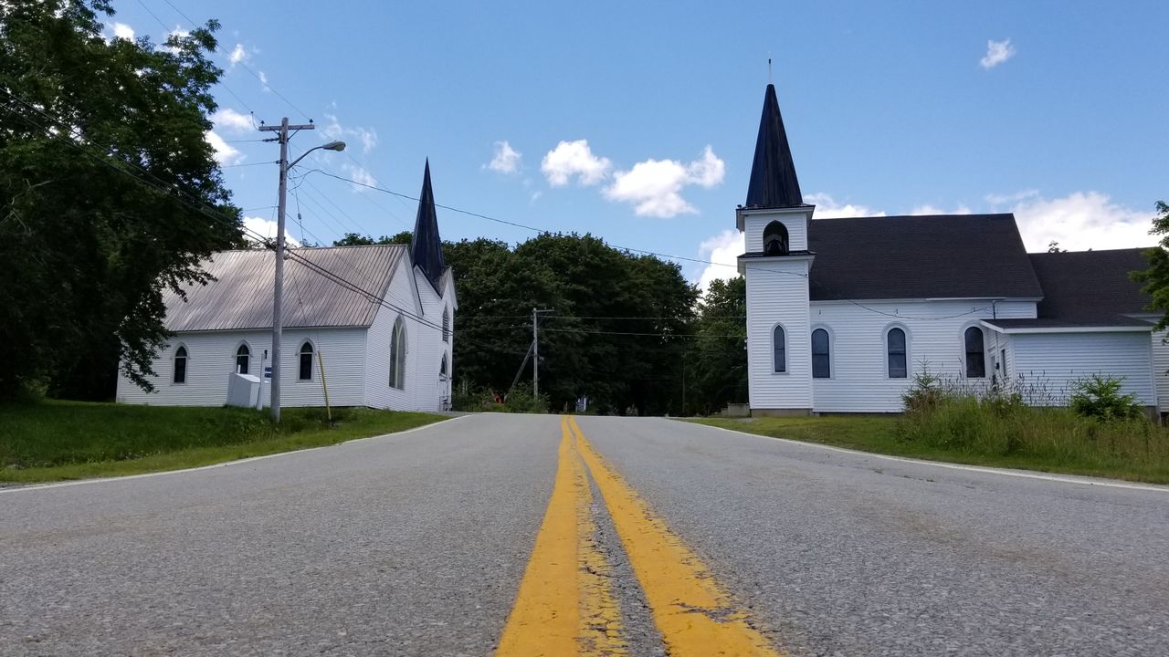 A serene rural road with classic white churches under a blue sky, ideal for peaceful scenery themes.
