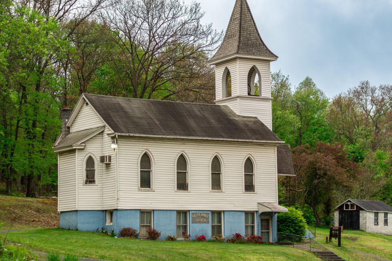 A quaint white church nestled amid lush green trees, evoking serenity in a rural setting.
